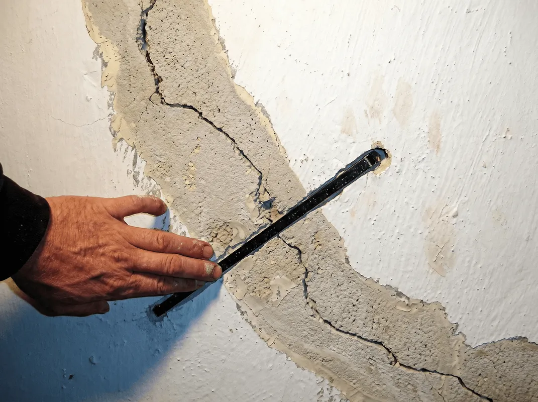 A wall with a large crack is being inspected by a professional in Manchester, NH